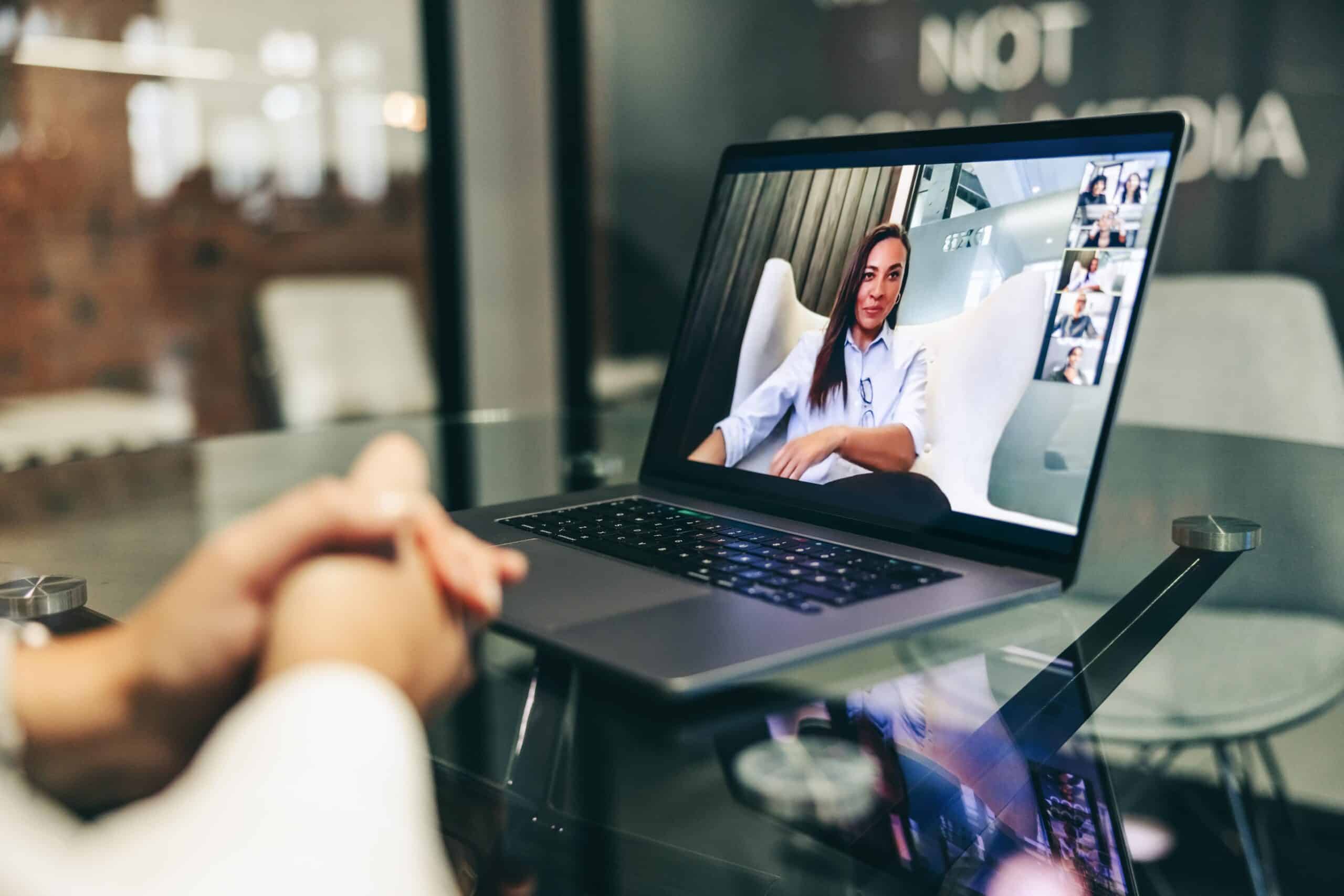 A professional black businesswoman engaged in a virtual meeting on her laptop screen within a contemporary and stylish office environment.